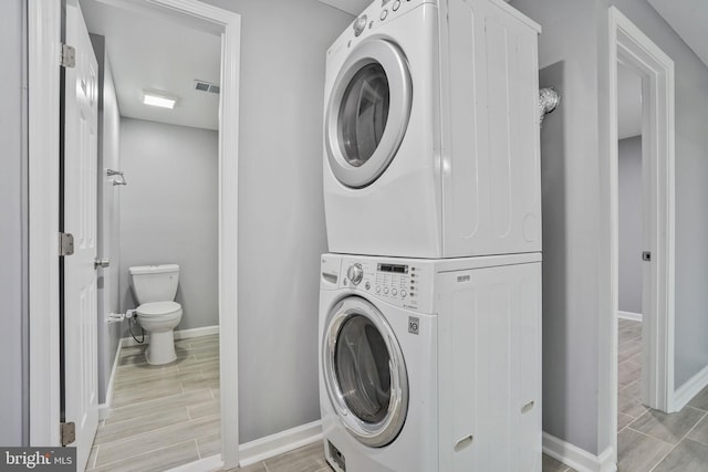 laundry room with laundry area, wood tiled floor, baseboards, and stacked washing maching and dryer
