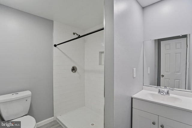 bathroom with toilet, a tile shower, and vanity