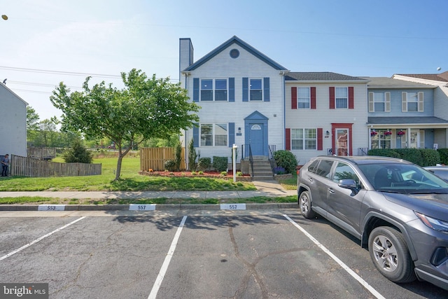 townhome / multi-family property featuring uncovered parking, fence, and a chimney