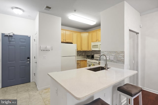 kitchen featuring a sink, light brown cabinets, white appliances, light countertops, and a peninsula