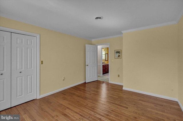 unfurnished bedroom with wood-type flooring, ornamental molding, baseboards, and visible vents