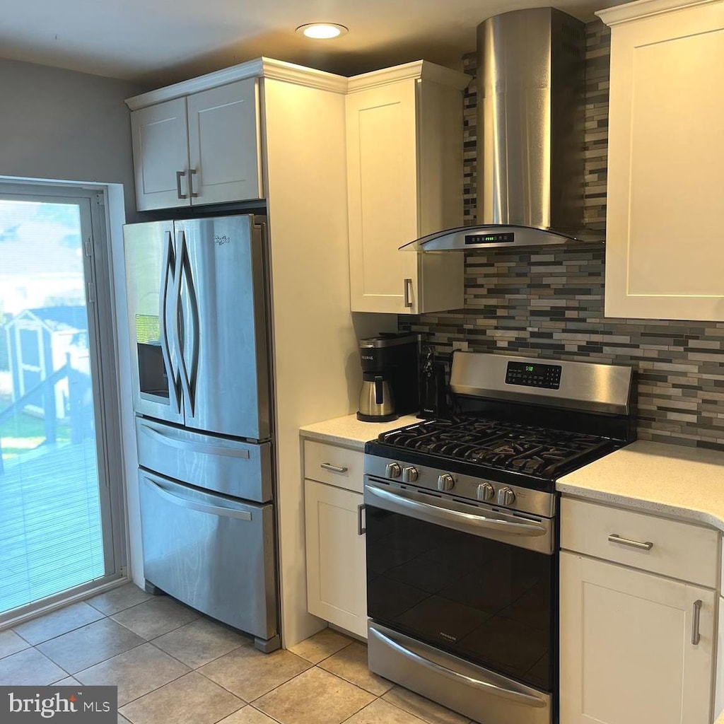 kitchen with wall chimney range hood, light tile patterned floors, stainless steel appliances, backsplash, and recessed lighting