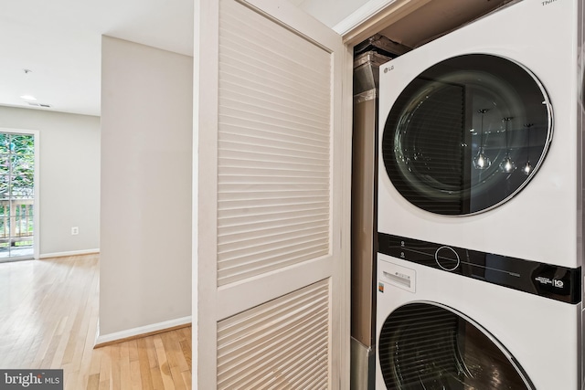 laundry area with baseboards, stacked washing maching and dryer, light wood-type flooring, and laundry area