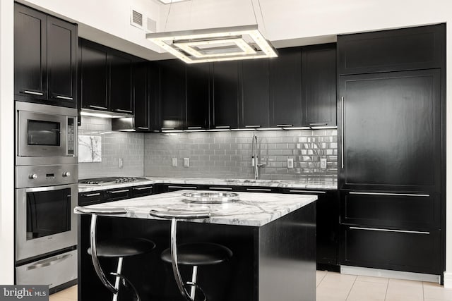 1414 S Penn Sq Unit 34B, Philadelphia, PA 19102 - kitchen featuring light tile patterned floors, appliances with stainless steel finishes, a center island, a warming drawer, and dark cabinetry