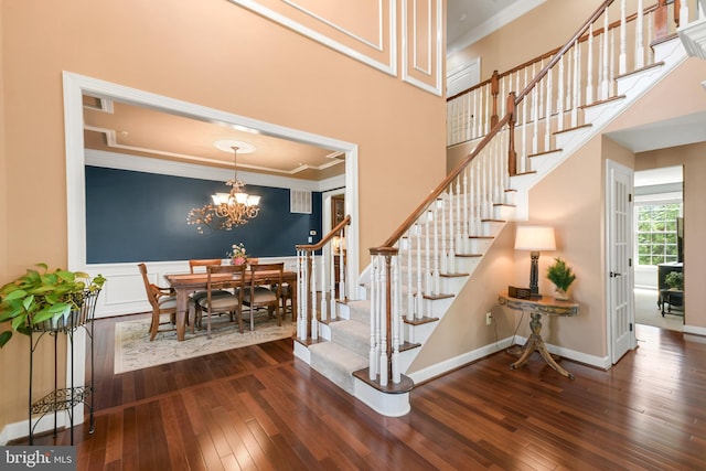 stairway with wood-type flooring, baseboards, crown molding, and an inviting chandelier