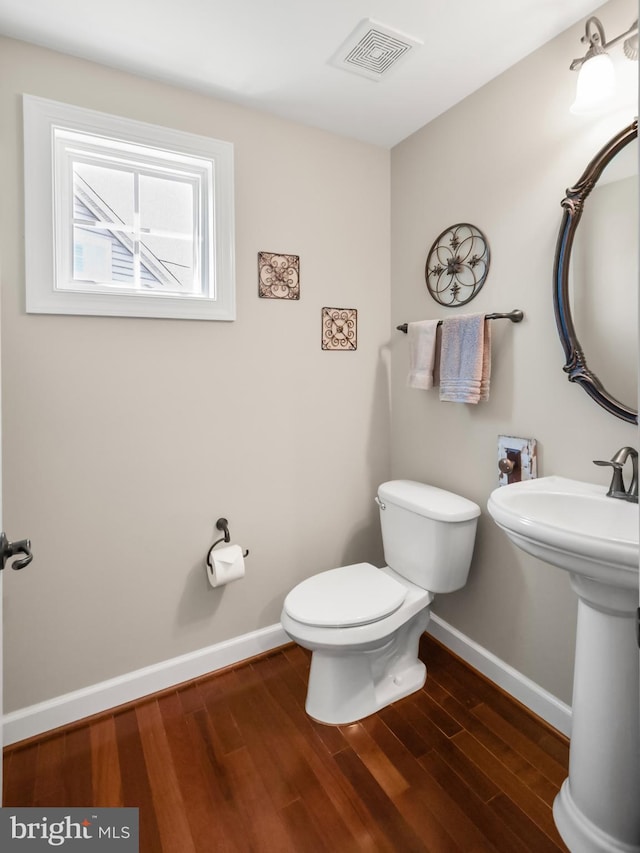 half bath with toilet, baseboards, visible vents, and wood finished floors