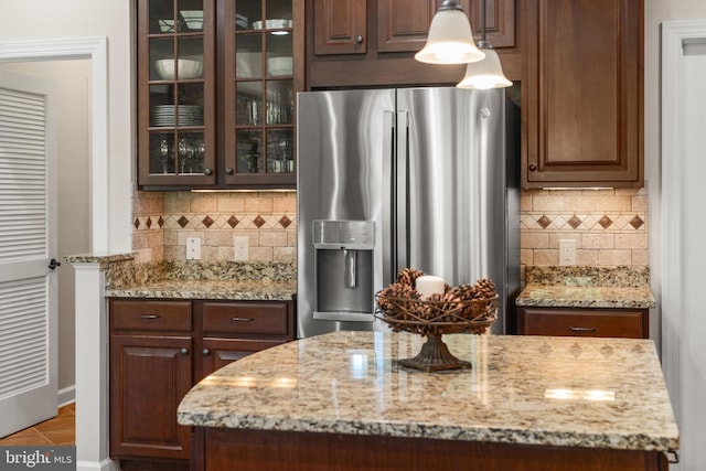 kitchen featuring backsplash, light stone counters, stainless steel fridge, and glass insert cabinets