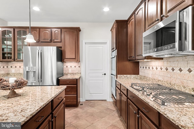 kitchen featuring hanging light fixtures, light stone counters, appliances with stainless steel finishes, tasteful backsplash, and glass insert cabinets