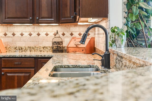 kitchen featuring dark brown cabinets, light stone countertops, a sink, and tasteful backsplash