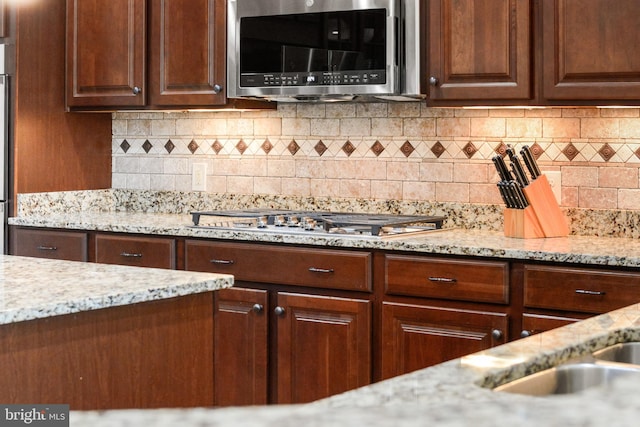 kitchen with appliances with stainless steel finishes, light stone counters, and tasteful backsplash