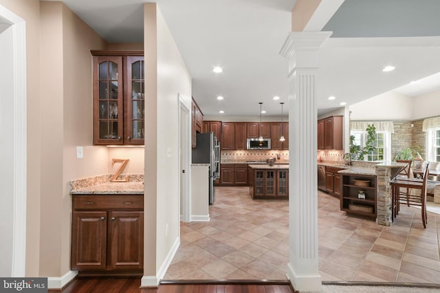 kitchen featuring tasteful backsplash, a sink, glass insert cabinets, stainless steel appliances, and ornate columns