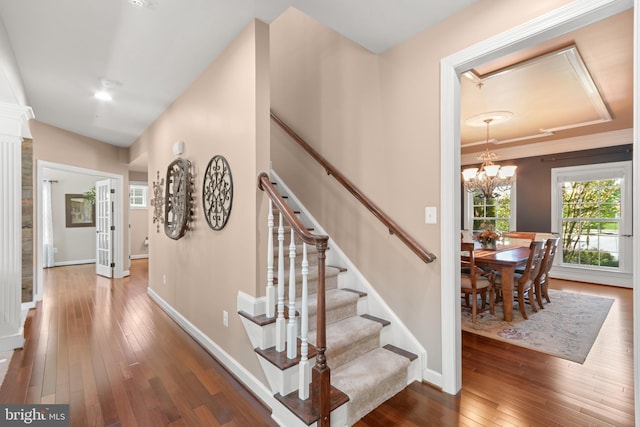 stairs with baseboards, decorative columns, hardwood / wood-style floors, and a chandelier