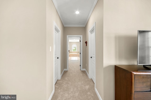 hall featuring crown molding, baseboards, and light colored carpet