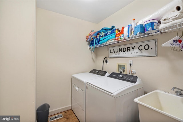 clothes washing area featuring light wood-style flooring, a sink, visible vents, separate washer and dryer, and laundry area
