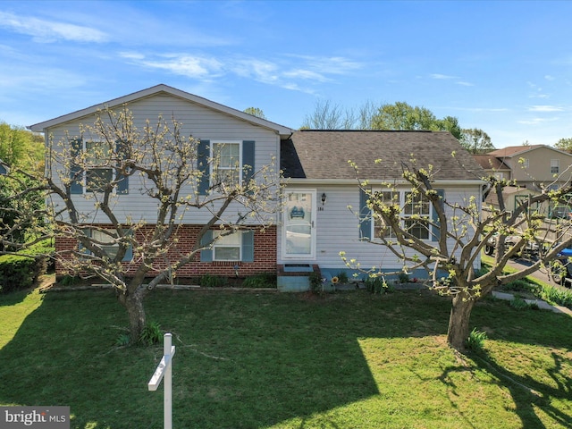 split level home with brick siding, roof with shingles, and a front lawn