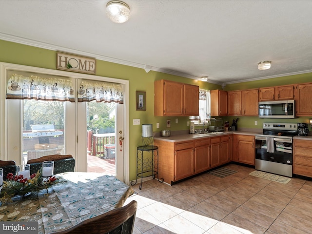 kitchen with crown molding, appliances with stainless steel finishes, a sink, light countertops, and light tile patterned flooring