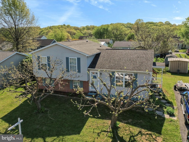 back of property featuring roof with shingles, a shed, brick siding, a lawn, and an outbuilding