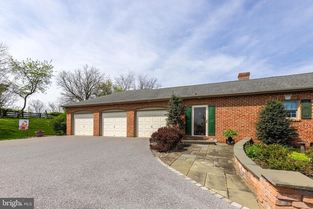 ranch-style house featuring a chimney, brick siding, a shingled roof, a garage, and driveway
