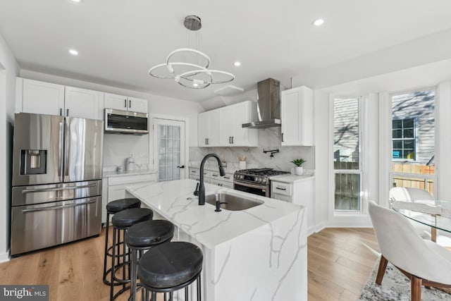 kitchen featuring wall chimney range hood, tasteful backsplash, a sink, stainless steel appliances, and a notable chandelier