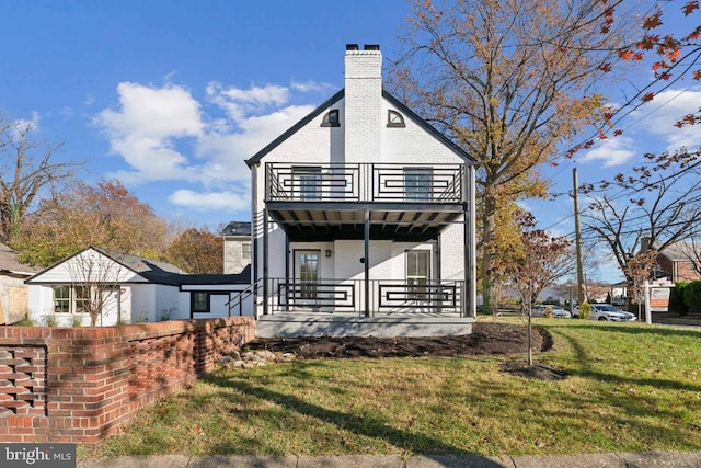 view of front of house featuring a chimney, covered porch, brick siding, a balcony, and a front yard