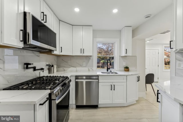 kitchen with light stone countertops, a sink, backsplash, white cabinets, and appliances with stainless steel finishes
