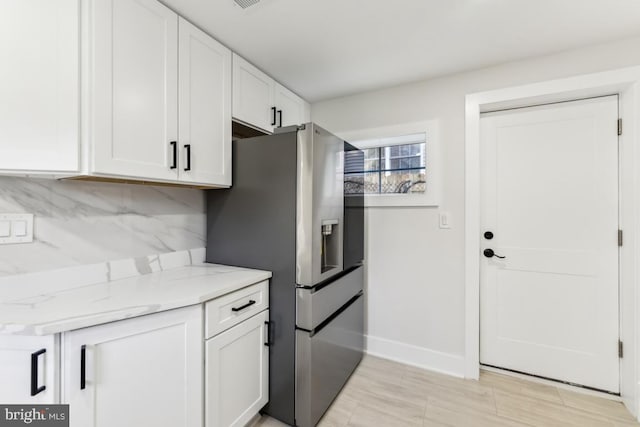 kitchen with baseboards, light stone countertops, stainless steel refrigerator with ice dispenser, and white cabinetry