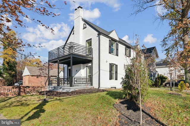back of property featuring a chimney, a yard, a balcony, and brick siding