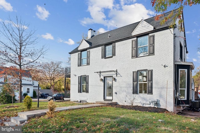 colonial house featuring a front lawn, a chimney, central AC, and brick siding