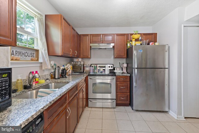 kitchen featuring appliances with stainless steel finishes, light stone countertops, a sink, under cabinet range hood, and light tile patterned flooring