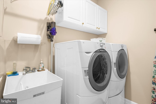laundry area with baseboards, washer and dryer, cabinet space, and a sink