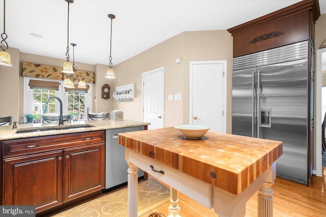 kitchen featuring light wood-style flooring, a sink, appliances with stainless steel finishes, butcher block countertops, and decorative light fixtures
