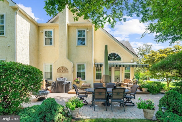 back of house featuring stucco siding, outdoor dining space, and a patio area