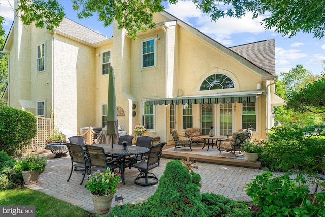 back of house with a shingled roof, stucco siding, and a patio area