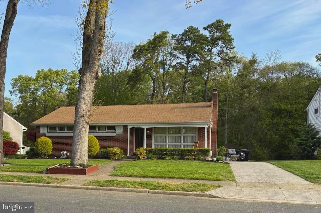ranch-style home featuring concrete driveway, brick siding, a chimney, and a front yard
