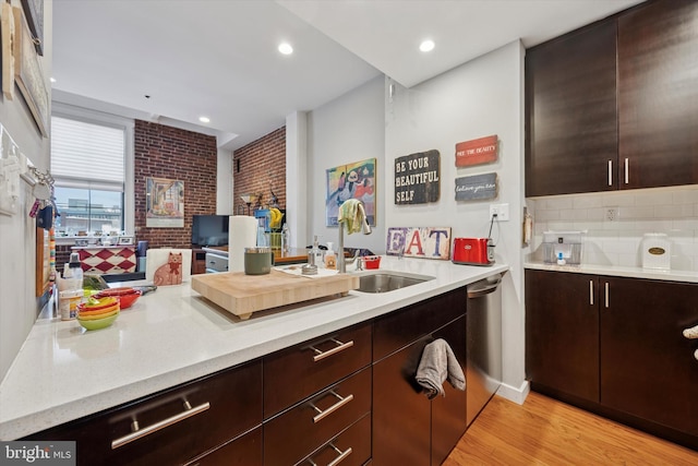 kitchen featuring dishwasher, light wood-style flooring, dark brown cabinets, brick wall, and decorative backsplash