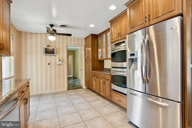 kitchen featuring appliances with stainless steel finishes, brown cabinets, stone countertops, and wallpapered walls