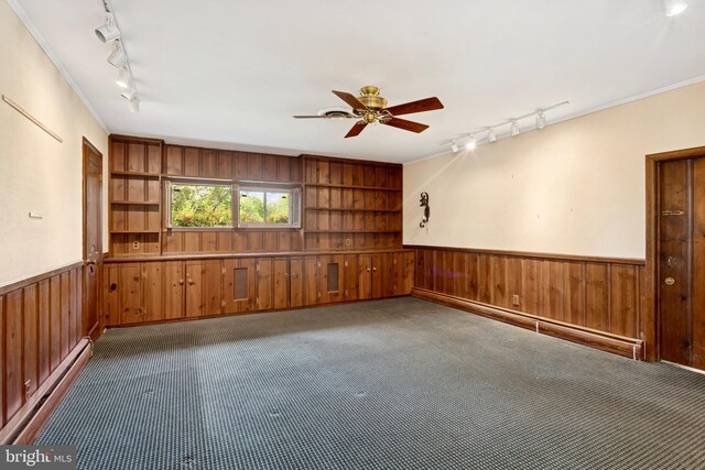 spare room with wood walls, dark colored carpet, a baseboard heating unit, and rail lighting