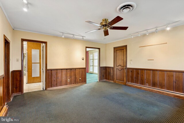 empty room with rail lighting, wainscoting, ceiling fan, and wooden walls