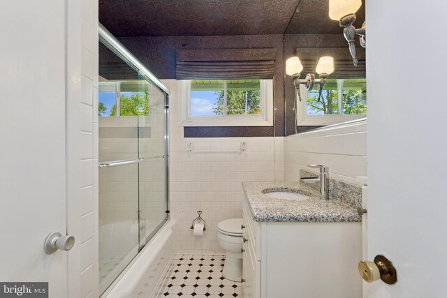 bathroom with vanity, toilet, tile walls, tile patterned floors, and combined bath / shower with glass door