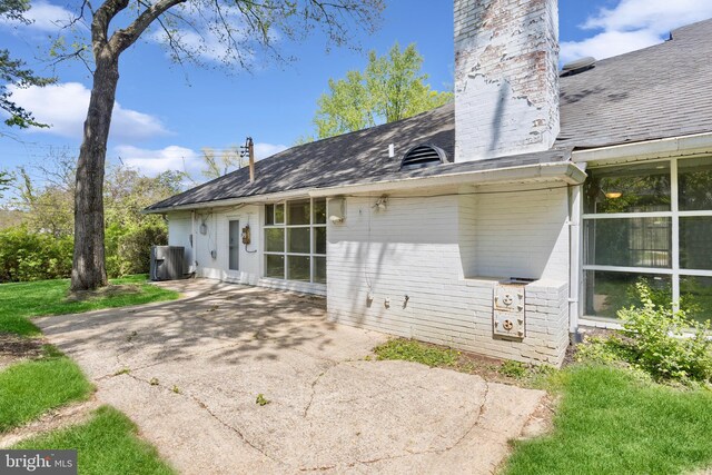 back of house featuring a shingled roof, a patio, a chimney, and brick siding