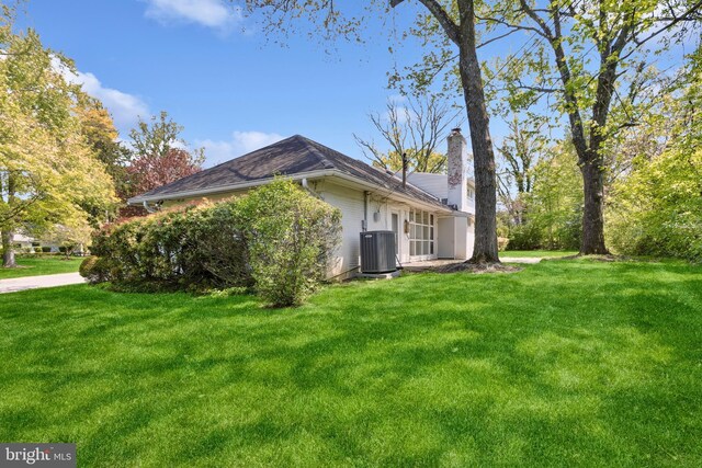 view of side of home with a lawn, central air condition unit, and a chimney