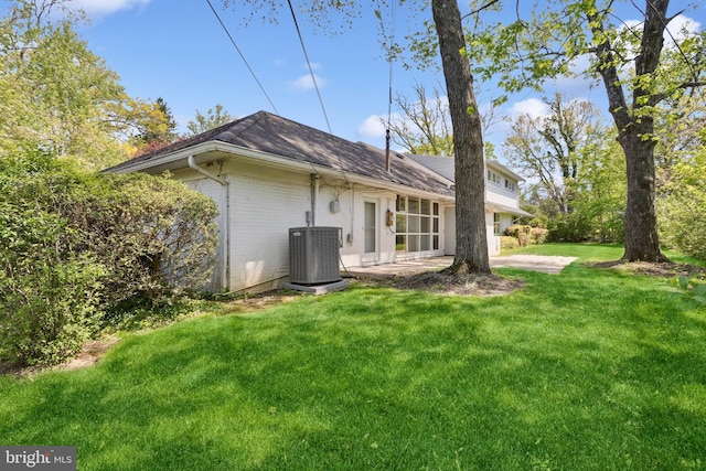 back of house featuring central AC, brick siding, a shingled roof, a patio area, and a yard
