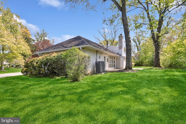view of side of property with central AC unit, a chimney, a yard, and brick siding