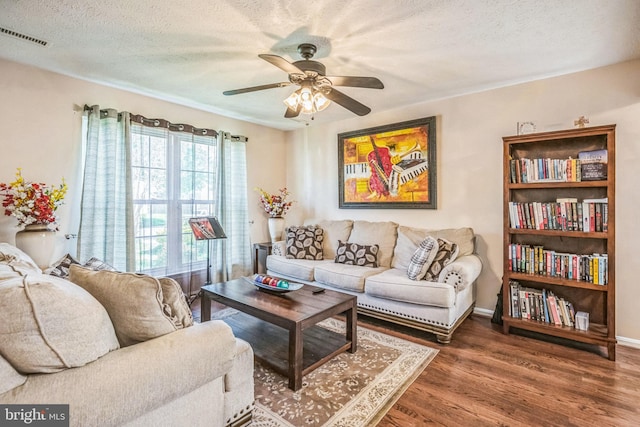 living room with a textured ceiling, visible vents, ceiling fan, and wood finished floors