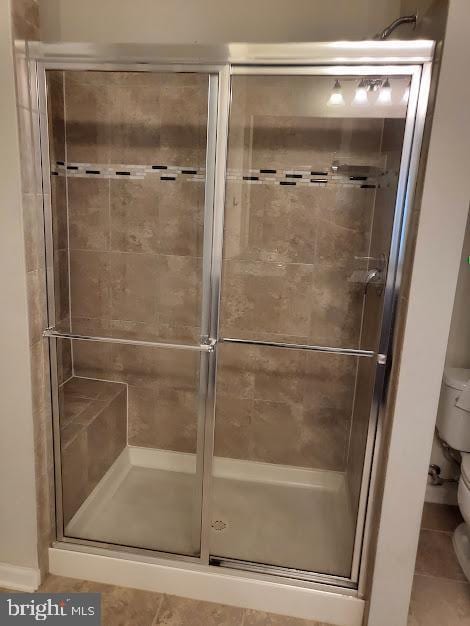bathroom featuring toilet, tile patterned flooring, a shower stall, and elevator