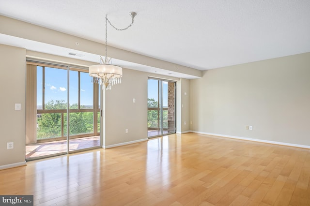 unfurnished room with a chandelier, light wood finished floors, and baseboards