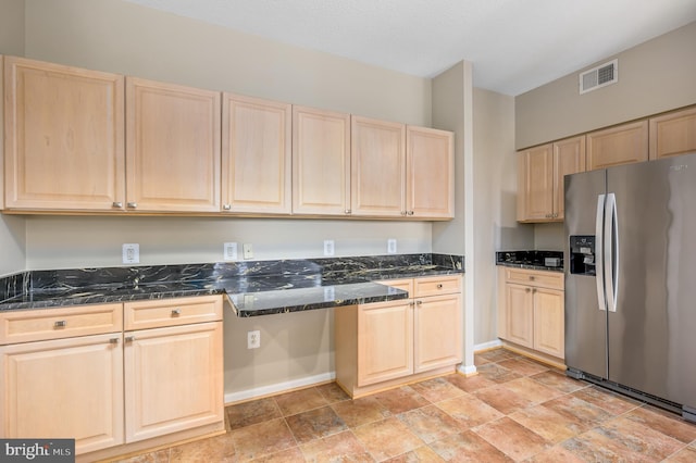 kitchen featuring stainless steel fridge with ice dispenser, light brown cabinetry, light stone finish flooring, dark stone countertops, and baseboards