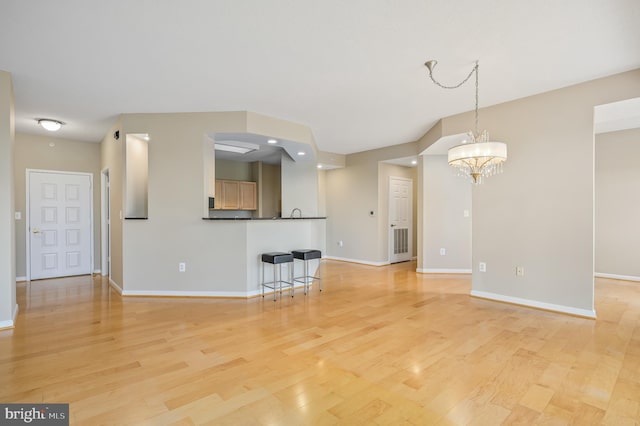 unfurnished living room with light wood-style floors, a chandelier, and baseboards