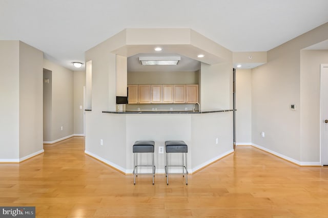 kitchen featuring light wood-style floors, baseboards, dark countertops, light brown cabinets, and recessed lighting