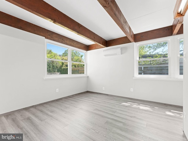 spare room with a wall mounted air conditioner, plenty of natural light, beam ceiling, and wood finished floors
